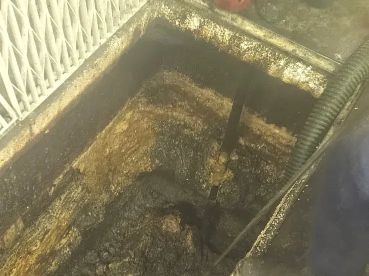 ASB Vac Services operator scraping and vacuuming a heavily crusted commercial grease arrestor