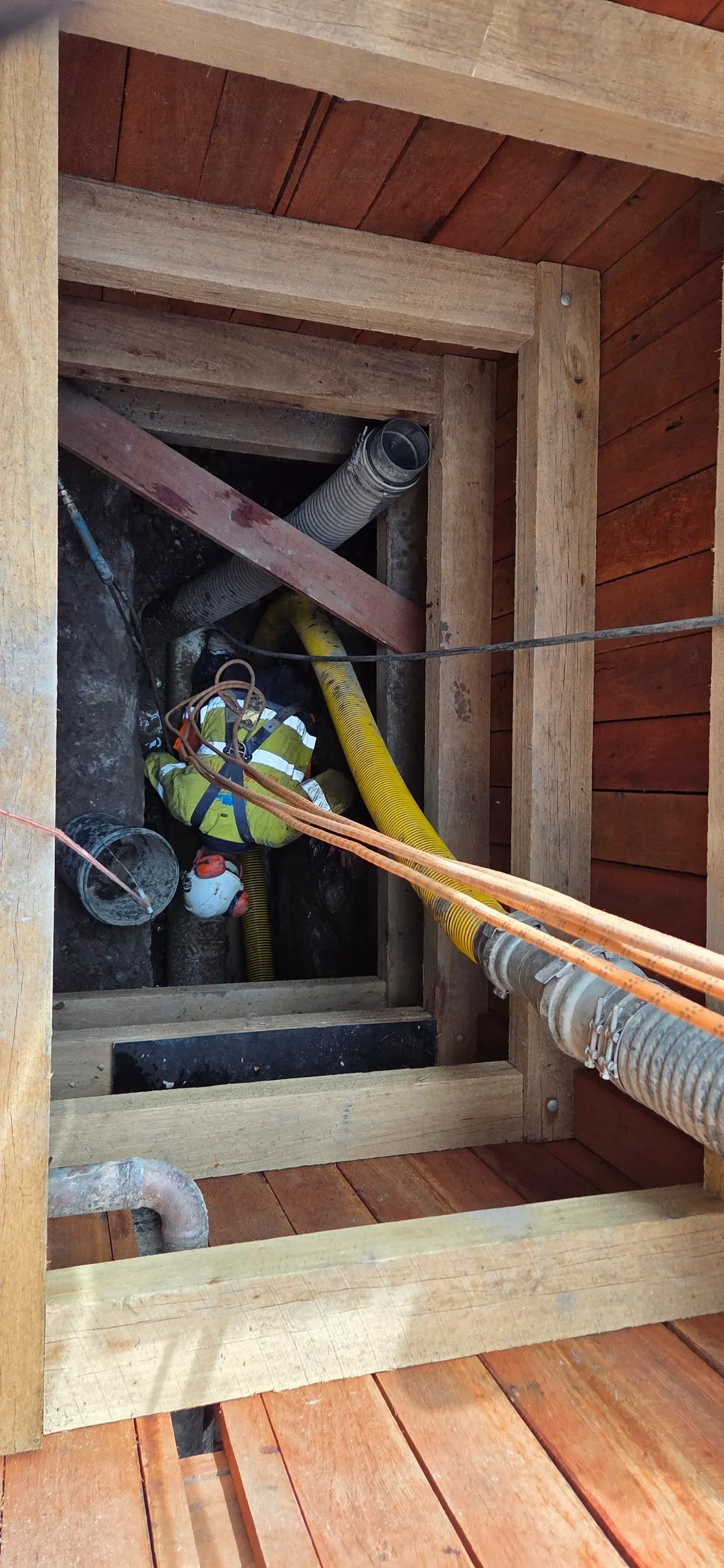 ASB Vac Services operator working in a timber-shored excavation with yellow vacuum hose — non-destructive digging in action